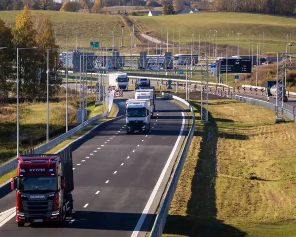 Ciężarówki na Via Baltica w jesiennym krajobrazie. Droga szybkiego ruchu z wieloma pojazdami, w tym czerwonym Scanią.