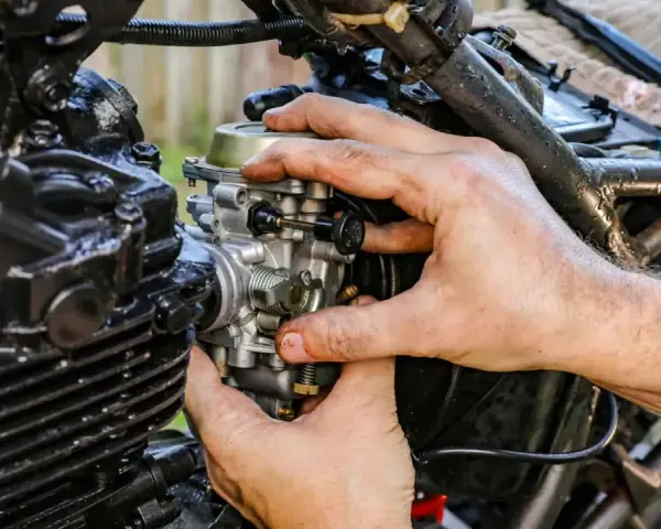 Dłonie mechanika regulują gaźnik motocykla, kluczowy element odpowiedzialny za symbol ssania paliwa i powietrza.