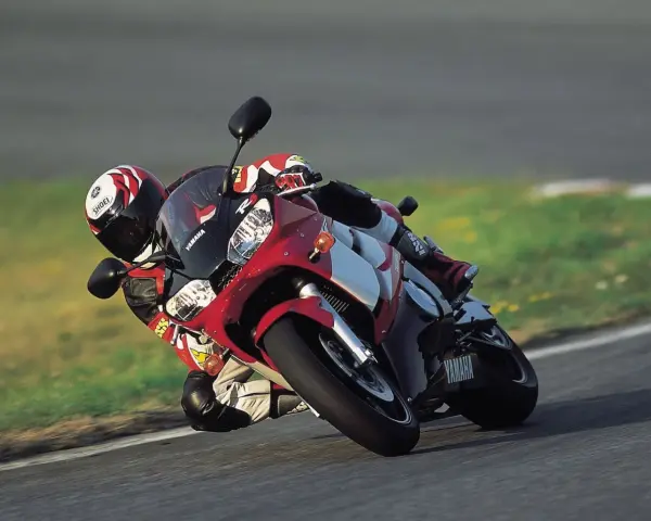 Motocyklista na torze pochyla się na swoim czerwono-białym motocyklu Yamaha R6 2001, w pełni ubrany w kombinezon i kask.