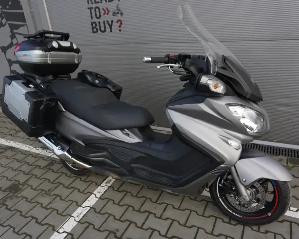 Srebrny Suzuki Burgman 650 Executive z kuframi, gotowy na dalekie podróże.