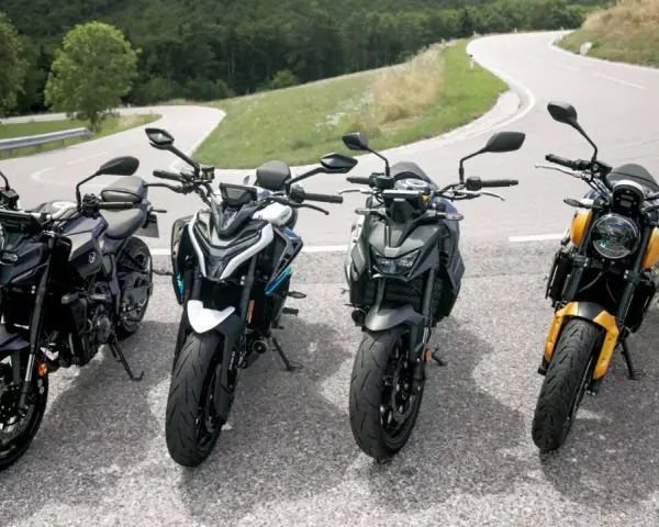 Cztery motocykle typu naked stojące na zakręcie górskiej drogi.