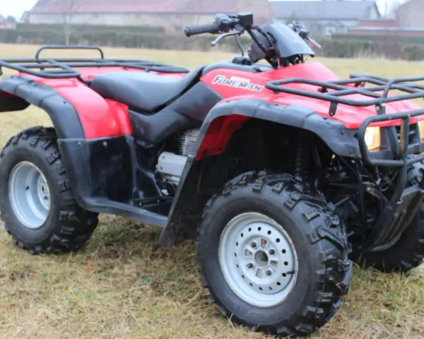 Czerwony quad Honda TRX 350 Foreman gotowy do jazdy po nierównym terenie.
