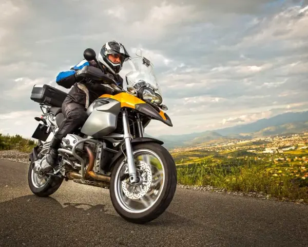 Motocyklista w kasku jedzie na motocyklu turystycznym. W tle rozciąga się malowniczy krajobraz z miastem. Zastanawiasz się nad koszt przerejestrowania motocykla?