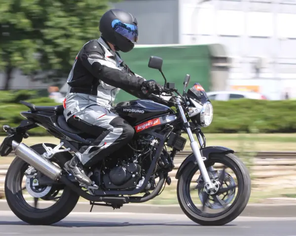 Motocyklista w kasku i kombinezonie jedzie na czarnym motocyklu Hyosung GT 125.