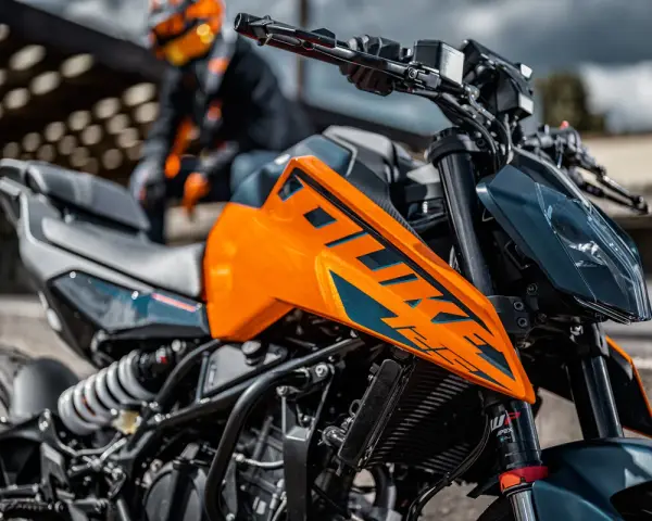 Pomarańczowy KTM Duke 390, zarejestrowany na 125, z motocyklistą w tle. Gotowy na przygodę!