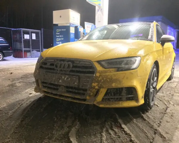 Żółte Audi na stacji benzynowej, pokryte błotem i śniegiem. Nieczytelna tablica rejestracyjna utrudnia identyfikację.