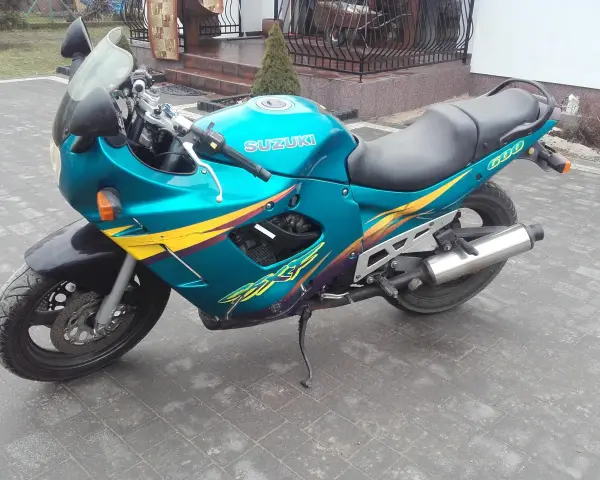 Turkusowy Suzuki GSXF 600 z żółto-fioletowymi grafikami, zaparkowany na kostce brukowej przed domem.