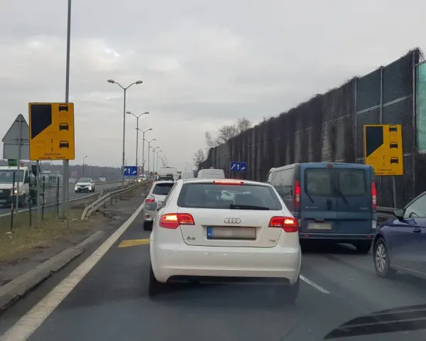 Korek na drodze, znaki informują o zalecanej zasadzie ruchu "na suwak". Unikaj mandatu, stosuj się do przepisów.