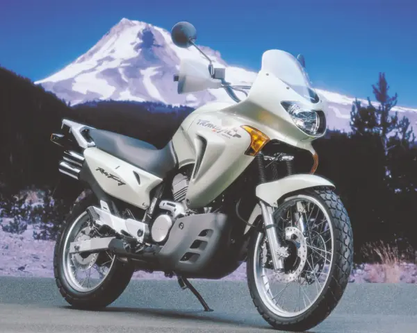 Srebrny motocykl Honda Transalp 650 gotowy na przygodę na tle ośnieżonej góry i lasu.