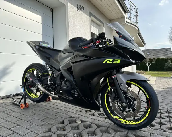 Czarny motocykl Yamaha R3 z żółtymi akcentami na felgach i owiewkach. Widać sportowy wydech Yoshimura. Idealny do poznania yamaha r3 dane techniczne.