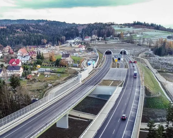 Nowa zakopianka trasa z tunelami i wiaduktami, otoczona lasami i zabudowaniami.