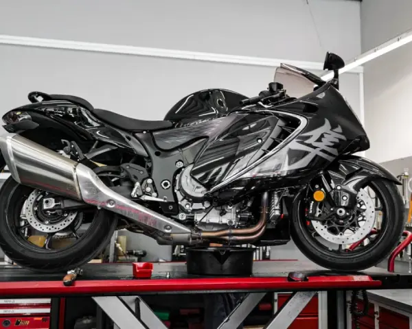 Czarny, lśniący motocykl typu naked bike na podnośniku w warsztacie. W tle tablica z narzędziami i napis "NAPRAWA".