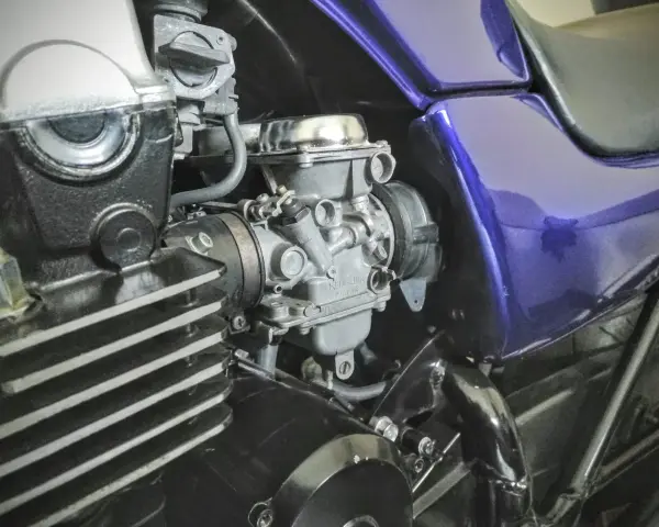 Szczegółowy widok gaźnika motocyklowego, kluczowego elementu układu dolotowego, z widocznymi przewodami i częściami silnika.