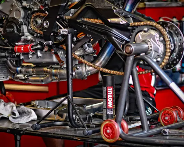 Motocykl na stojaku, widoczny napęd i łańcuch. Puszka smaru Motul sugeruje, co ile smarować łańcuch w motocyklu.
