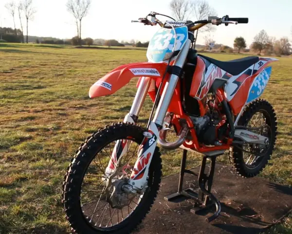 Pomarańczowy motocykl KTM SX 125 na stojaku, gotowy do jazdy. Zastanawiasz się, ile koni ma KTM SX 125? Ten model to potęga na torze!