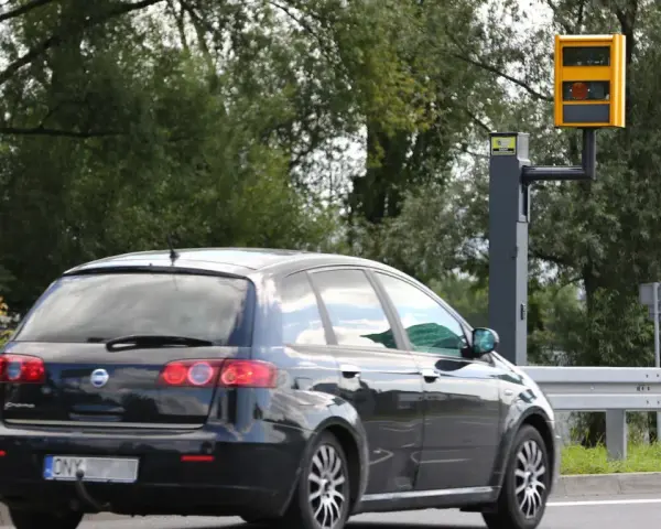 Czarny samochód mija fotoradar. Kierowca motocykla powinien uważać na ograniczenie prędkości.
