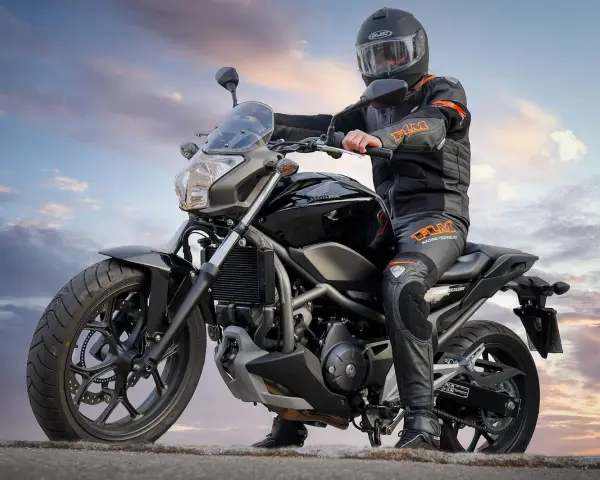 Motocyklista w kasku i kombinezonie siedzi na czarnym motocyklu. Idealny motor na kat B, gotowy na przygodę.