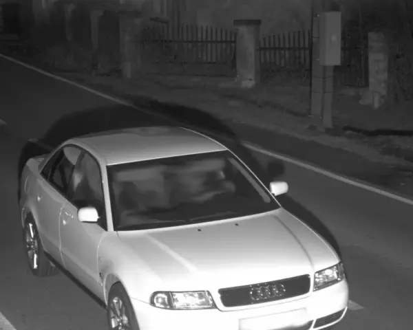 Biały sedan Audi przejeżdża przez nocne zdjęcie z fotoradaru.