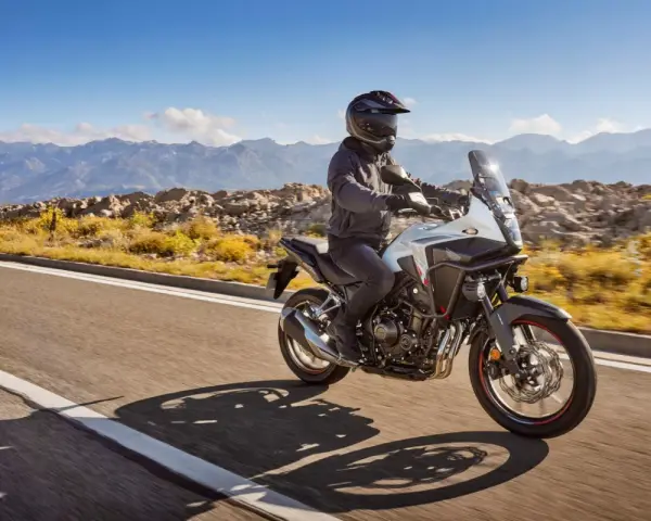 Motocyklista na białym Honda CB500X przemierza malowniczą, górską drogę.