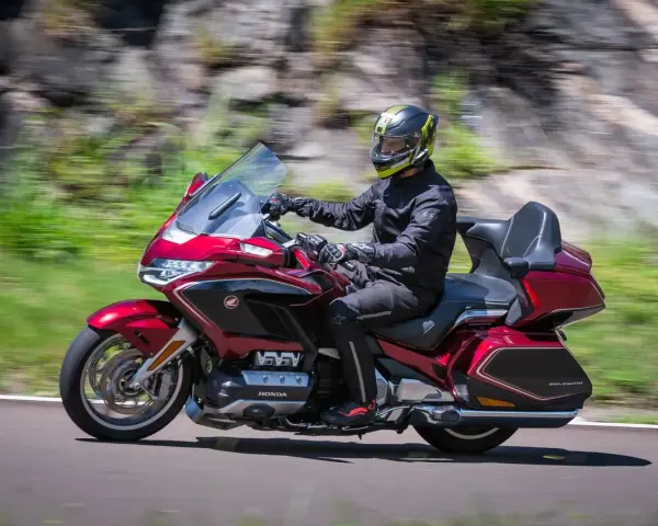 Mężczyzna w kasku jedzie lśniącym, czerwonym motocyklem Honda Gold Wing, uznawanym za najlepszy motocykl turystyczny.