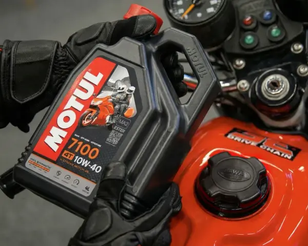 Rękawice motocyklisty trzymają olej Motul 7100 10W-40. Pytanie: co ile wymieniać olej w motocyklu?