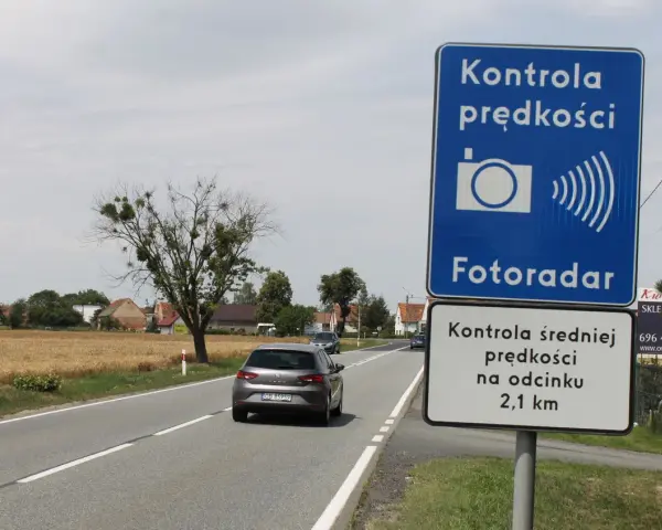 Znak "Kontrola prędkości Fotoradar" informuje, że czy fotoradar musi być oznakowany. Obok droga i pola.