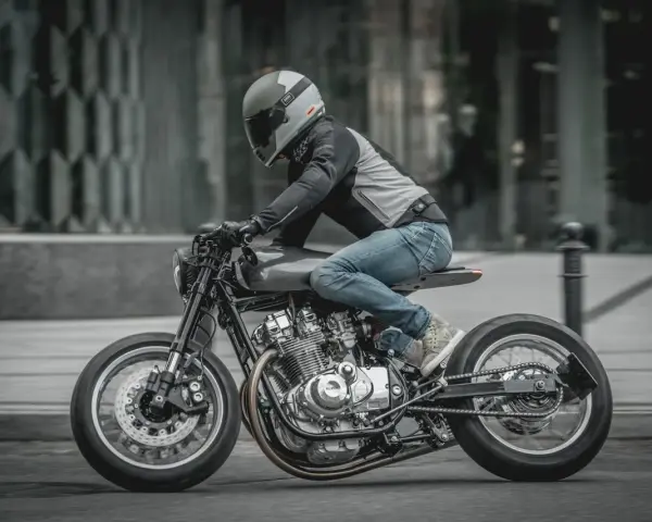 Motocyklista w kasku i jeansach pędzi na stylowym Suzuki GS 650 po miejskiej ulicy.