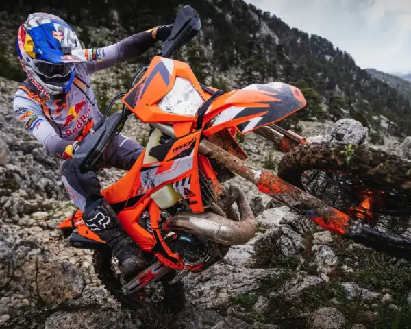 Motocyklista w kasku Red Bull na pomarańczowym KTM EXC 300 2T pokonuje kamienisty teren. Dane techniczne tego potwora terenowego są imponujące.
