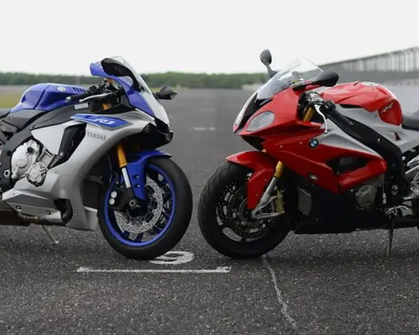 Dwa sportowe motocykle: niebiesko-srebrny Yamaha R1 i czerwono-biały BMW S1000RR 2020, stojące na torze wyścigowym.