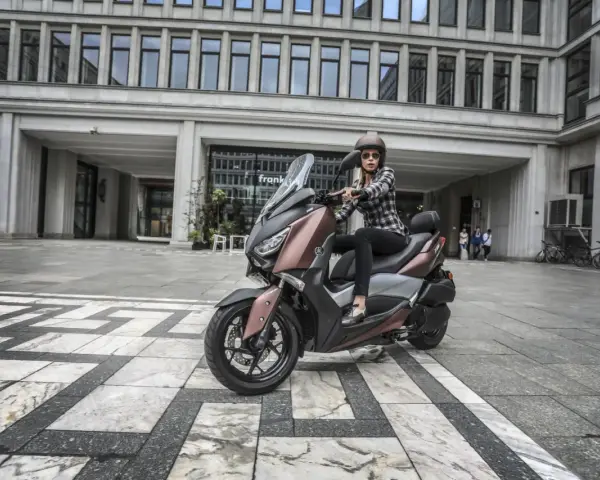 Kobieta na skuterze Yamaha X-MAX 300, gotowa do jazdy. Zastanawia się, jaka będzie jej prędkość maksymalna w mieście.