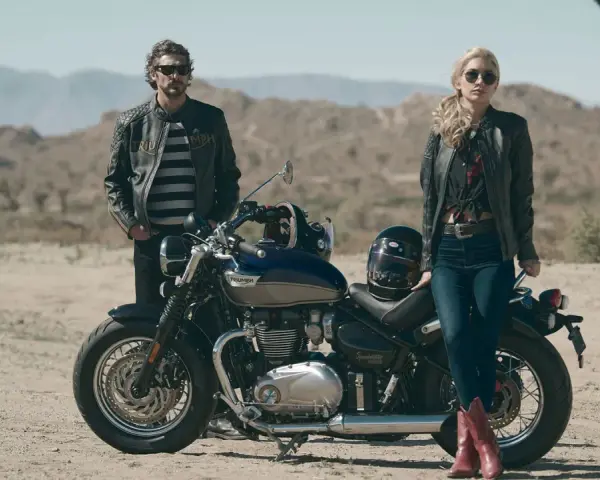 Para w skórzanych kurtkach pozuje przy motocyklu Triumph Speedmaster na pustynnym tle.