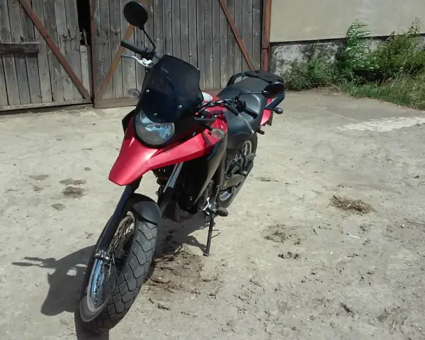 Czerwony motocykl Derbi Terra 125 stoi przed drewnianą stodołą.
