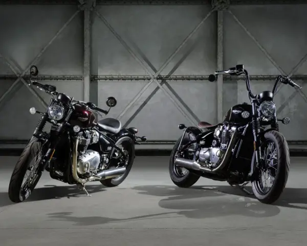 Dwa motocykle Triumph Bonneville Bobber w ciemnych kolorach, stojące obok siebie w industrialnym wnętrzu.