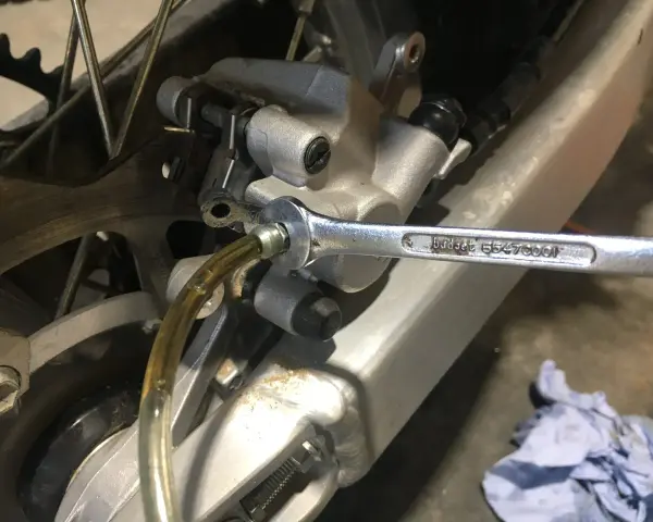 Klucz nasadowy odkręca odpowietrznik podczas czyszczenia hamulców motocykla. Płyn hamulcowy spływa przez przezroczysty wężyk.