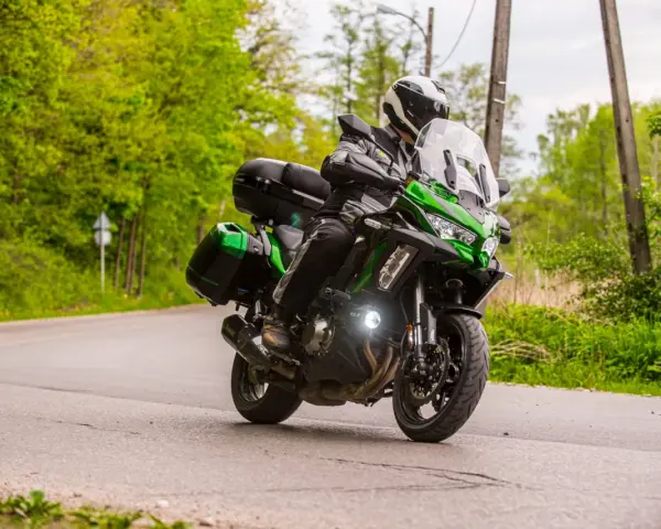 Motocyklista na zielonym Kawasaki Versys 1000, z kuframi, pokonuje zakręt. Nawet z potencjalnymi wadami, jazda nim to przygoda.