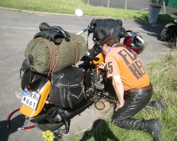 Motocyklista sprawdza uszkodzony gaźnik objawy. Na motocyklu sakwy, zielony worek i czarne rękawice.