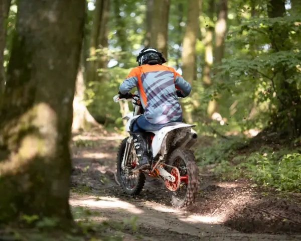 Motocyklista w kasku i kolorowej bluzie pędzi leśnym szlakiem. Od ilu lat można jeździć crossem? Odpowiedź zależy od przepisów i umiejętności.
