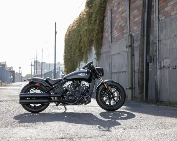 Czarny motocykl typu cruiser Indian Scout stoi na ulicy, z zielonym bluszczem zwisającym ze ściany w tle.
