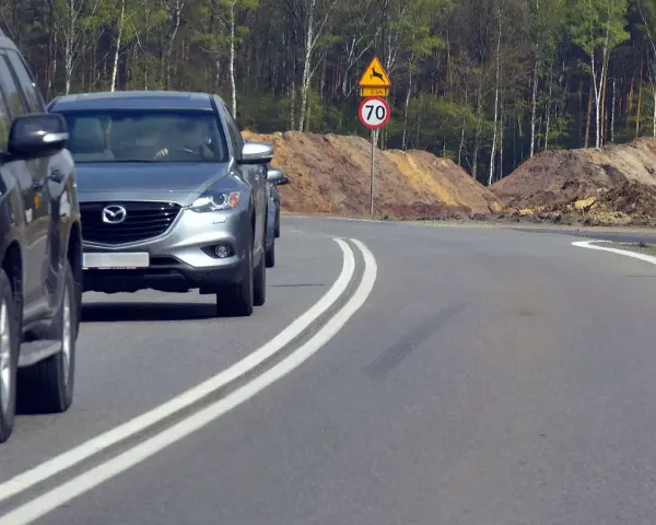 Kierowca próbuje wyprzedzanie na podwójnej ciągłej, ignorując znak ograniczenia prędkości do 70 km/h i ostrzeżenie o dzikich zwierzętach.