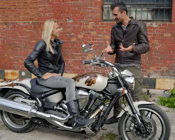 Kobieta siedzi na motocyklu Yamaha Warrior 1700, mężczyzna obok opowiada o jego możliwościach.