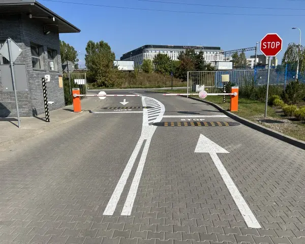 Przed wjazdem na teren, gdzie obowiązuje znak P-15, stoją szlabany. Na drodze namalowano strzałki kierunkowe i napis STOP.