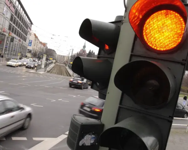 Żółte światło na sygnalizatorze drogowym, ruch uliczny i budynki w tle.