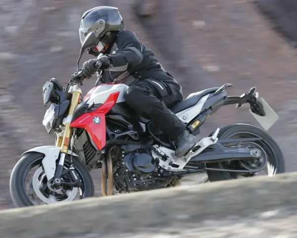 Motocyklista w kasku i kombinezonie pędzi na motocyklu BMW F900R po kamienistym terenie.