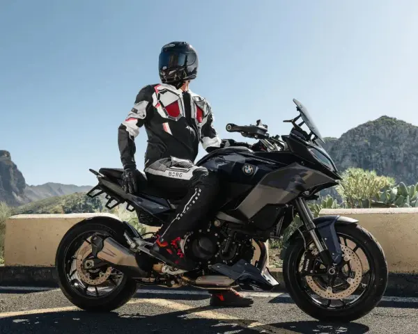 Motocyklista w kombinezonie na czarnym motocyklu BMW, gotowy do podróży po górskich drogach. Wśród wielu marek motocykli, ta prezentuje się imponująco.