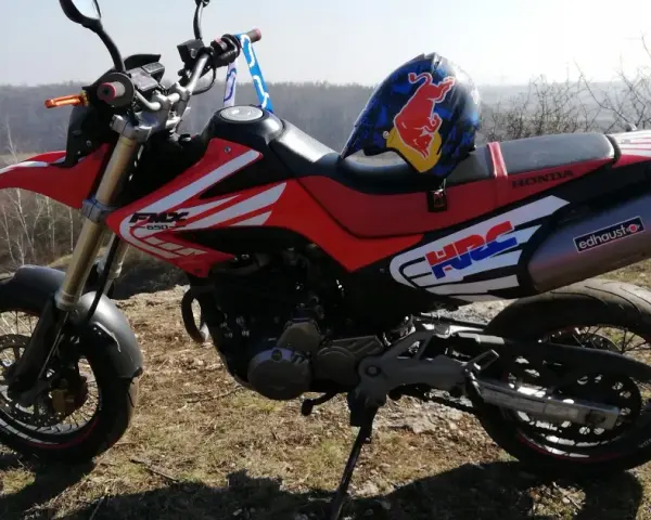 Czerwony motocykl Honda FMX 650 z kaskiem Red Bull na siedzeniu, gotowy na przygodę w terenie.