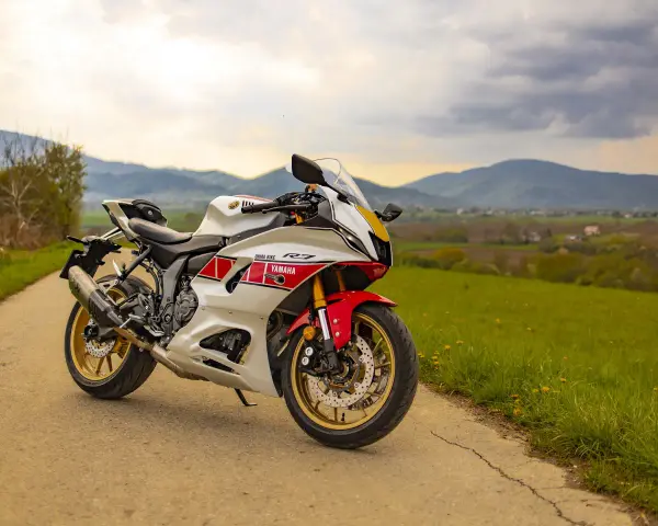 Sportowy motocykl Yamaha R7 w białym malowaniu z czerwonymi akcentami, zaparkowany na drodze wśród zielonych wzgórz. Sprawdź aktualną yamaha r7 cena!