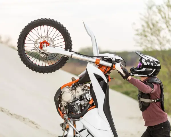 Motocyklista w kasku i ochraniaczach wykonuje wheelie na piaskowej wydmie. To najszybszy cross na świecie, gotowy do akcji.