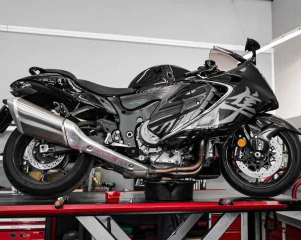 Czarny motocykl na podnośniku, gotowy do serwisu. Widać duży, chromowany wydech, który odcina się od reszty maszyny.