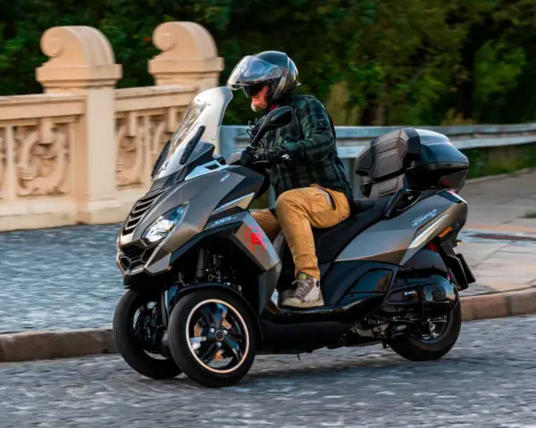 Mężczyzna w kasku jedzie trójkołowym skuterem Peugeot Metropolis 400. Widoczna jest jego prędkość maksymalna.