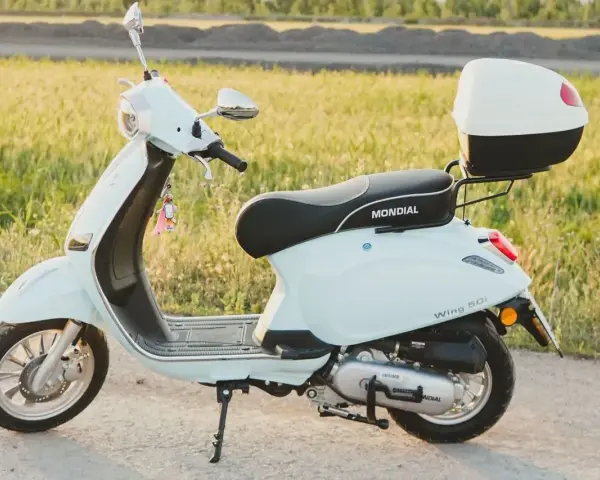 Jasny skuter Mondial Wing 50i, idealny na pierwsze przejażdżki bez prawa jazdy, stoi na tle zielonego pola.